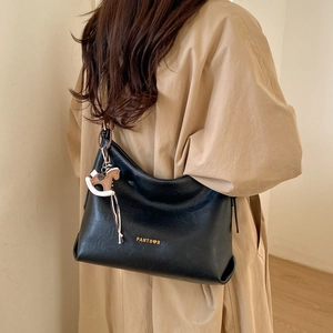 Detail of black leather tote bag with gold logo and decorative horse pendant