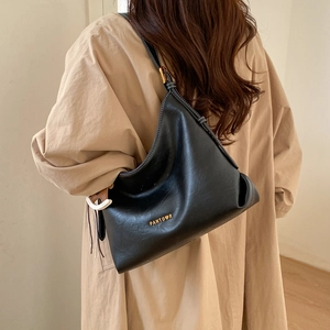 Detail of a black leather hobo tote bag worn with a stylish tan trench coat