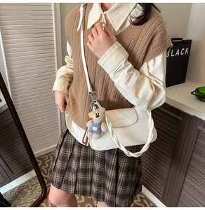 Close-up of a white leather crossbody bag with a plush bear charm and woven handle detail
