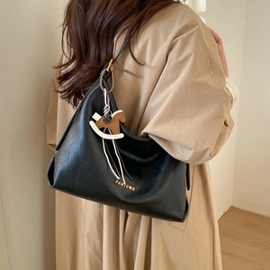 Close-up of black tote bag with gold logo and horse charm worn on khaki coat