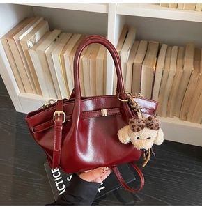 Detailansicht der weinroten Handtasche mit glatter Textur und niedlichem Plüsch-Anhänger