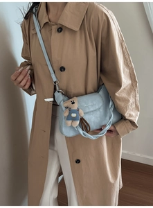 Detail of light blue crossbody bag with braided handle and cute brown bear pendant