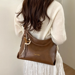 Detail of a large dark brown leather tote bag with a gold logo and rocking horse charm