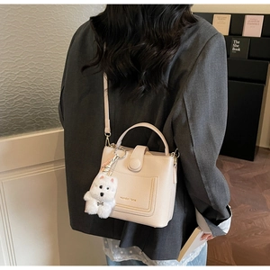 Détail du sac seau beige à motif litchi avec breloque chien en peluche et logo doré