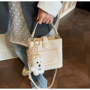 Détail du sac seau beige en cuir grainé avec un porte-clé en peluche en forme de chien