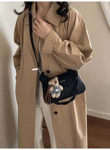 Detail of black leather crossbody bag with braided handle and bear plush charm on model