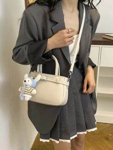 Elegante borsa a secchiello in pelle crema con manico e ciondolo a orsetto su modella