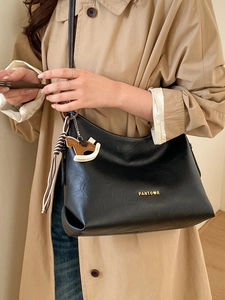 Black leather tote bag with gold logo and wooden horse charm on a trench coat model
