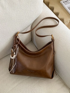 Brown leather hobo bag with adjustable strap and horse charm on a beige sofa