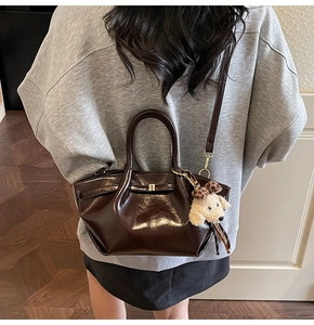Detail einer dunkelbraunen Lackledertasche mit Plüschwelpen-Anhänger an einem Modell