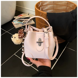 Detail of light pink bucket bag with silver twist lock and plush bear charm accent
