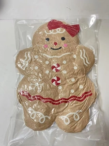 Detail of gingerbread man plush pillow with red bow and peppermint buttons in packaging
