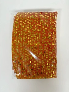 Detailaufnahme von orangefarbenem Paillettenstoff mit goldenem Glanz in Verpackung
