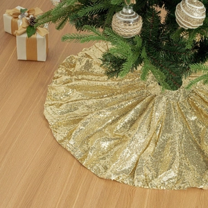Sparkling gold sequin Christmas tree skirt on light wooden floor with festive gift box