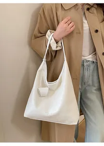 Dettaglio di una borsa tote in pelle bianca lucida indossata con un trench kaki casual