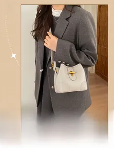 Macro view of cream-colored pebble leather bucket bag with gold T-shaped metal buckle