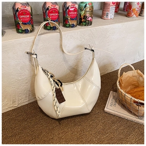 Dettaglio della borsa hobo a mezzaluna crema con cuciture patchwork e ciondolo al cioccolato