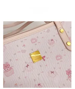 Detail of pink cartoon tote bag showing textured leather and golden metal logo plate