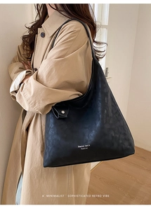 Detail of minimalist black hobo tote bag featuring pebbled leather texture and brand logo