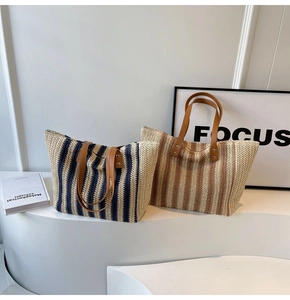 Close-up of woven straw tote bags with contrast stripes and leather handles on white pedestals