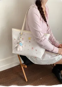 Detail of printed tote bag with white plush puppy charm and floral cartoon patterns