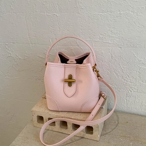 Detail of pink lychee leather bucket bag with gold cross twist lock on stone block