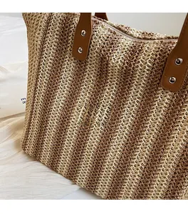 Detail of striped straw tote bag showing contrast weave, leather handles and metal studs