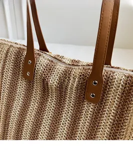 Close-up of woven straw tote bag featuring brown faux leather straps and silver metal rivets