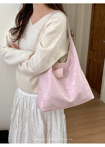 Close-up of pink pearlescent leather tote bag with decorative tag worn on shoulder