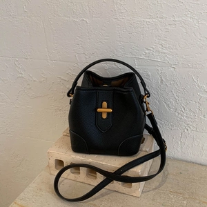 Close-up of black litchi pattern bucket bag with golden cross buckle and leather handle