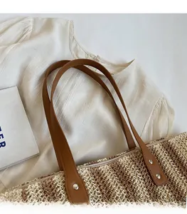 Detail of woven straw tote bag featuring brown leather handles and silver metal rivets