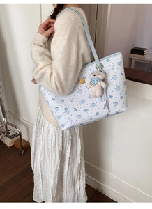 Detail of printed white tote bag featuring blue bear patterns and a plush bear charm