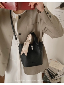Detail of black lychee grain leather bucket bag with silver lock and decorative silk scarf