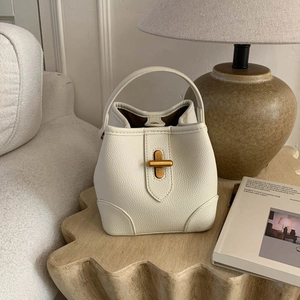 Detail of cream white leather bucket bag with gold metal twist lock on wooden table