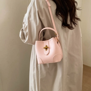 Detailed back view of a pink bucket bag with gold cross-lock on a beige trench coat