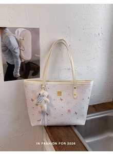 Detail of cream tote bag with pink cartoon bear patterns and white plush charm accessory
