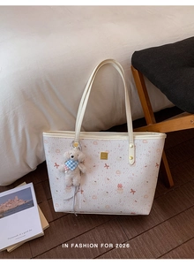 Close-up of cream tote bag with pink ribbon print and plush dog charm on wooden floor