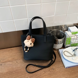 Detail of black pebbled leather tote bag with a cute plush bear charm and long strap