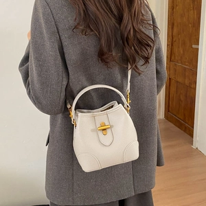 Detail of a creamy white textured leather bucket bag with golden cross metal lock and strap