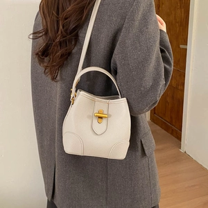 Detail of off-white lychee grain bucket bag featuring a golden T-shaped metal twist lock