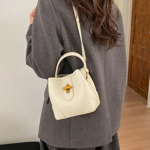 Detail of a creamy white leather bucket bag with gold hardware worn as a crossbody