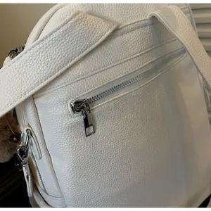 Close-up of smooth silver zipper on white lychee grain leather backpack back pocket