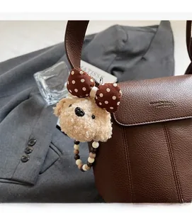 Detail eines Plüschbären-Anhängers mit gepunkteter Schleife an brauner Ledertasche