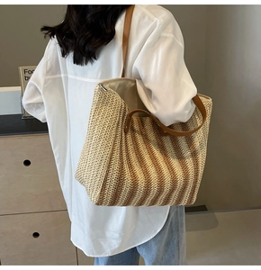 Detailed view of a woven straw tote bag with brown straps worn on a shoulder