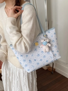 Light blue tote bag with cartoon bear prints and cute plush charm shown on shoulder