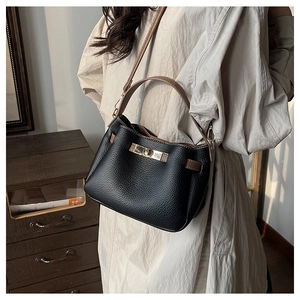 Détail du sac seau noir en cuir grainé avec lanière marron et fermoir doré rotatif
