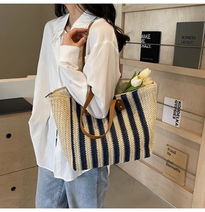 Detail of striped straw tote bag featuring brown leather straps and top zipper closure