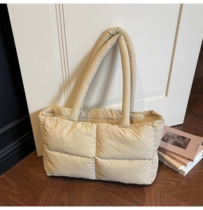 Detail of beige quilted puffer tote bag leaning against a door in a stylish room