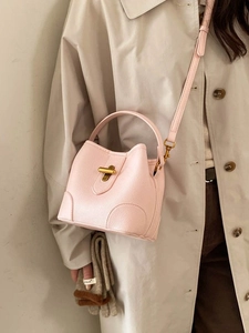 Pink lychee texture bucket bag with gold hardware and adjustable strap on a trench coat