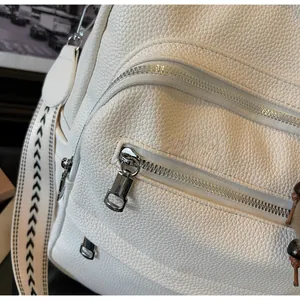 Detail of smooth silver zippers and lychee grain leather texture on white backpack